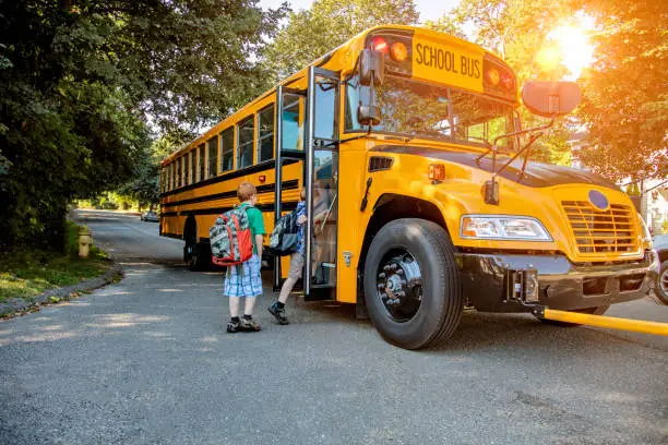 A young redheaded boy getting onto a school bus in sunshine