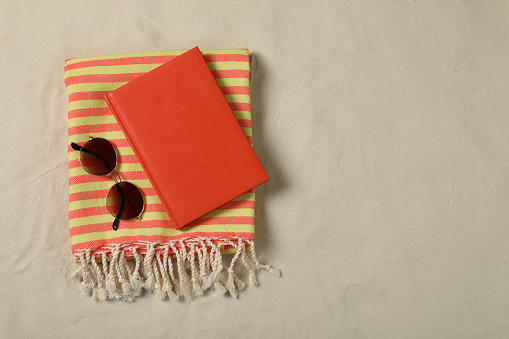 Beach towel, book and sunglasses on sand, top view. Space for text
