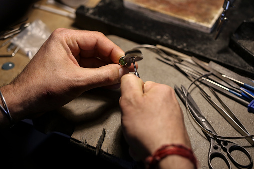 Close-up of an unrecognizable male Caucasian jeweller polishing a ring in his workshop.