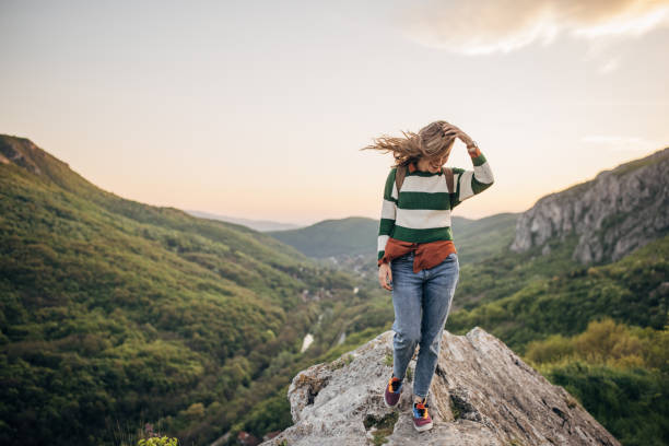 One woman, young female hiker standing on a rock high on mountain in sunset.