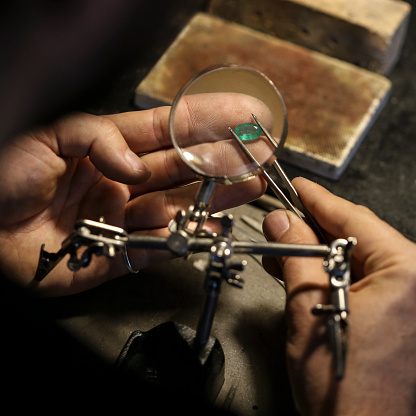 Close-up of an unrecognizable male Caucasian jeweller analyzing an emerald gemstone in his workshop.