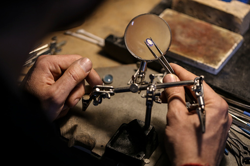 Close-up of an unrecognizable male Caucasian jeweller analyzing a gemstone in his workshop.