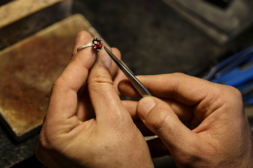Close-up of an unrecognizable male Caucasian jeweller working on a ruby ring in his workshop.