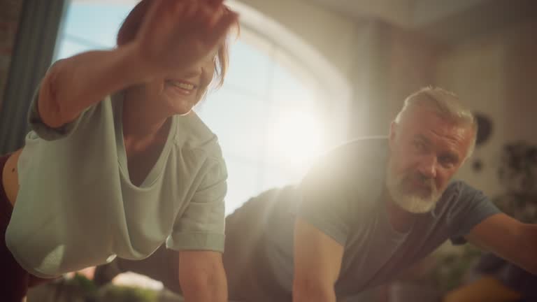 Portrait of a Senior Couple Doing Gymnastics and Yoga Stretching Exercises Together at Home on Sunny Morning. Concept of Healthy Lifestyle, Fitness, Recreation, Couple Goals, Wellbeing and Retirement.