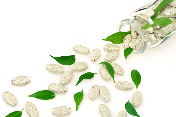 Herbal supplement pills and fresh leaves  spilling out of bottle stock photo