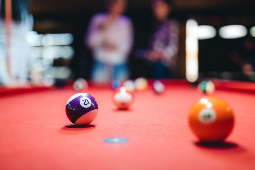 Close up of number 10 snooker ball on pool table with people in the background.