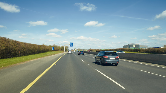 Rear view of cars driving on motorway, Ireland. Road with metal safety barrier or rail. cars on the asphalt under the cloudy blue sky. Highway traffic.