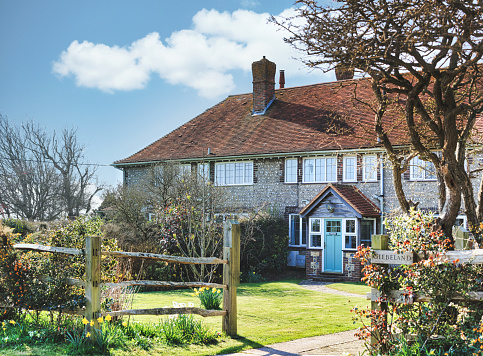 East Dean, Eastbourne, England - March 24, 2022: Colour image depicting the exterior of a traditional detached English house in the countryside, with a freshly manicured lawn and garden, East Dean, Eastbourne, England.