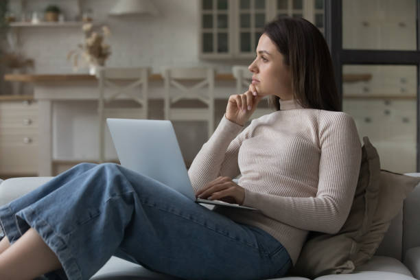 donna premurosa seduta sul divano con il laptop che fissa via - topics selective focus concepts blog foto e immagini stock