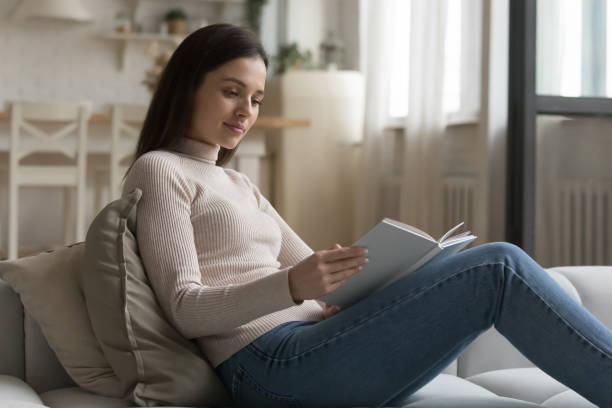 istock Young woman relax on couch spend leisure reading a book 1395762521