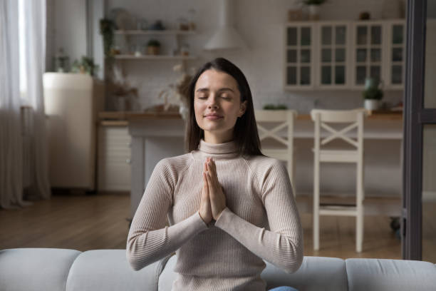 istock Young woman prays seated on sofa at home 1395762555