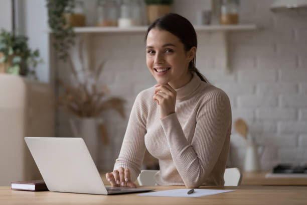 istock Woman sit at table with laptop smile look at camera 1395762586
