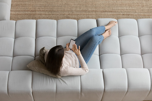 Overhead view young woman relax on cozy sofa spend leisure alone at home use smartphone, white mock up on device screen, make order online via electronic service. Modern tech, mobile app usage concept