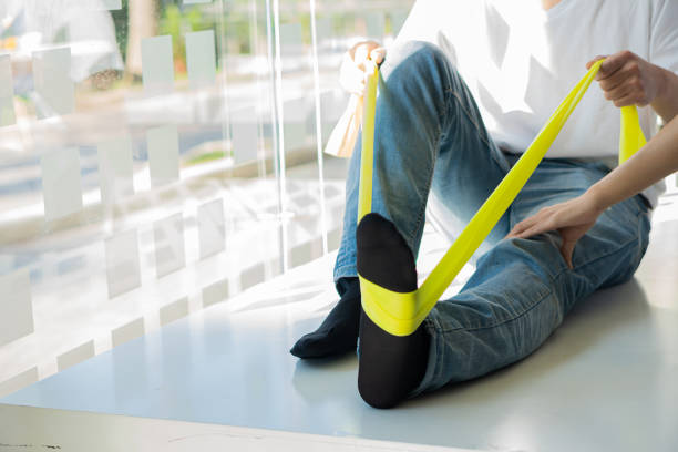 istock rehabilitation therapy A physical therapist assists a patient while stretching his leg with a green-yellow hose and works with a young male patient in a rehabilitation center. 1395764721