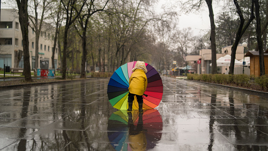 Happy Child With Rainbow Umbrella Under Rain