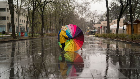 Cute boy with colorful rainbow umbrella on rainy