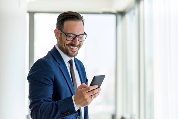 gut aussehender geschäftsmann, der smartphone benutzt und lächelt - businessman stock-fotos und bilder