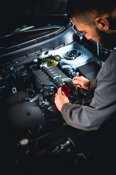 Focused mechanic doing car repair. Disconnecting the battery terminal of modern car. Vertical photography. stock photo
