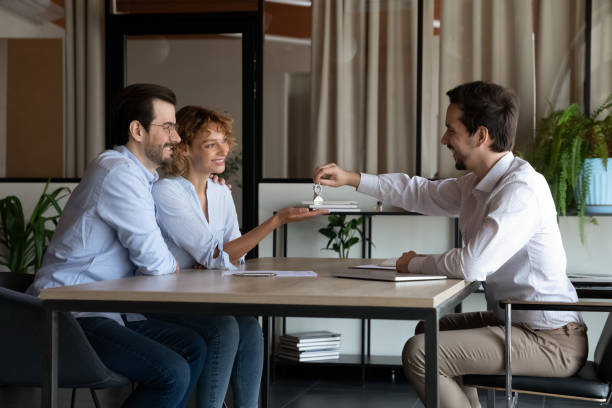 Real Estate Agent giving key from first home to happy family couple Real Estate Agent giving key from first home to happy family couple of clients. Married customers meet with real estate agents, house sellers, and landlords in the office for property buying or rent deals. Landlords And Property Owners stock pictures, royalty-free photos & images.