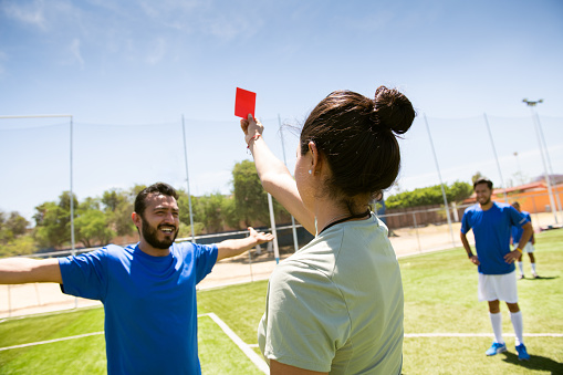 Female refree showing red card to complaining soccer player