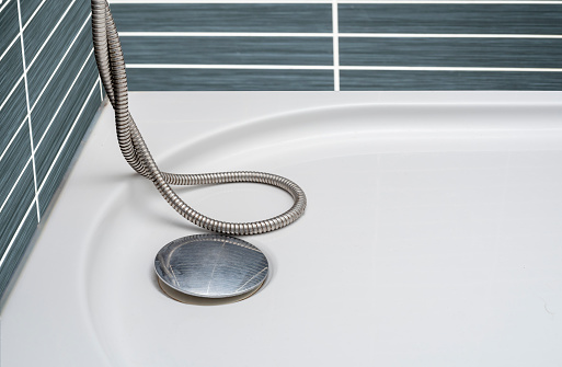 A closeup of a white porcelain bathtub situated at an angle on a ceramic tiled floor, with a wooden chair nearby
