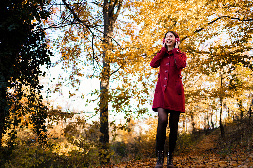 Woman in red coat listening to music while walking through the woods