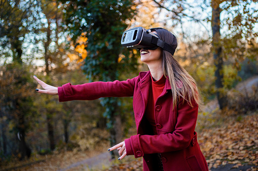 Woman in red coat experiencing virtual reality while walking in the nature