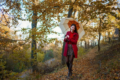 Smiling woman in red coat with umbrella on a beautiful autumn day walking in the woods