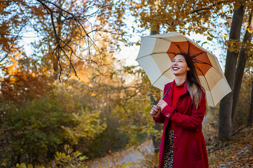 Smiling woman in red coat with umbrella on a beautiful autumn day walking in the woods