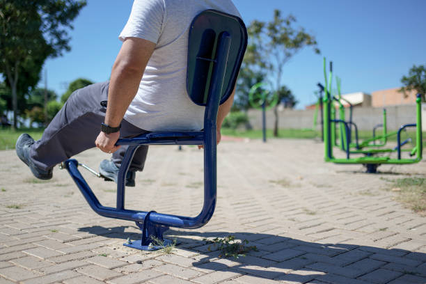 Portrait of a young man exercising at a park, in a non urban city, surrounded by trees and a summer blue sky. He is exercising on the bicycle, getting in shape.