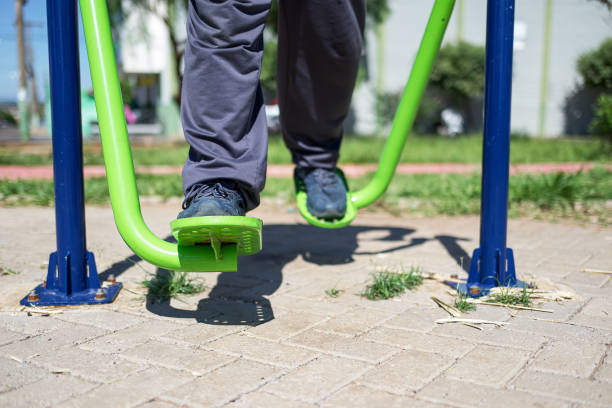 Portrait of a young man exercising at a park, in a non urban city, surrounded by trees and a summer blue sky. He is exercising on a walking device, getting fit.