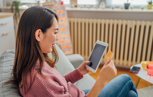 Young smiling Japanese woman using tablet for online shopping at home