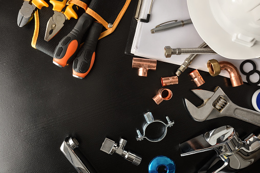 Concept of plumbing industrial technical service and revisions with notepad and tools and plumbing material on black table. Top view. Horizontal composition.