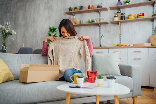 Happy young Japenese woman unpacking clothes after online shopping