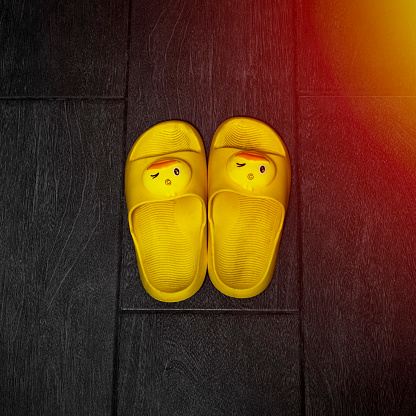 Pair of yellow children's slippers in the form of winking ducks on the wooden floor of the bathhouse close-up.
