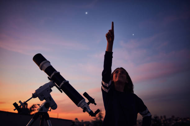 istock Girl with astronomical telescope stargazing under twilight sky. 1395787186
