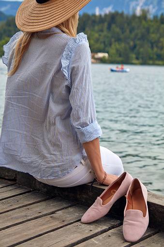 Young adult tourist woman enjoying barefoot on a lake wooden pier.