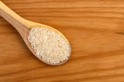 Close up view of white rice on wooden spoon on table in the kitchen