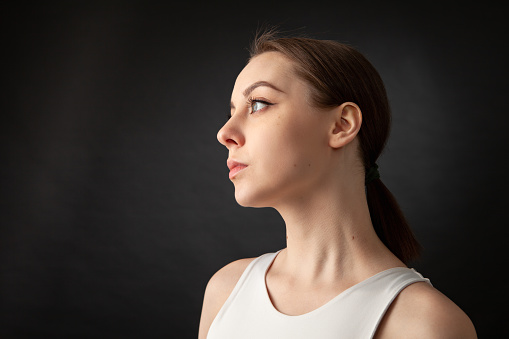 Close-up studio portrait of an attractive 20 year old woman with brown hair in a white tank top on a black background