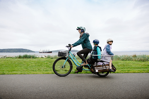 A multiracial family biking on a large electric powered cargo bicycle, perfect for commuting for the environmentally conscious.  Also a fun, healthy family activity that provides good exercise!  Shot in Tacoma, Washington, USA.