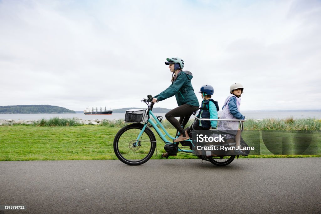 Bike Ride on Cargo E-Bike Carries The Whole Family A multiracial family biking on a large electric powered cargo bicycle, perfect for commuting for the environmentally conscious.  Also a fun, healthy family activity that provides good exercise!  Shot in Tacoma, Washington, USA. Electric Bicycle Stock Photo