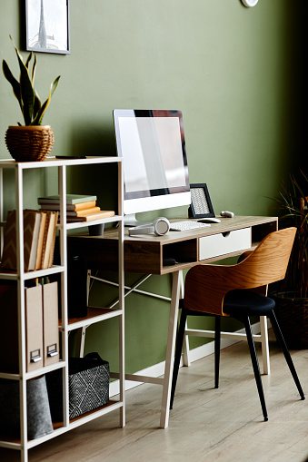 Full length background image of home office workplace with computer on wooden table against green wall