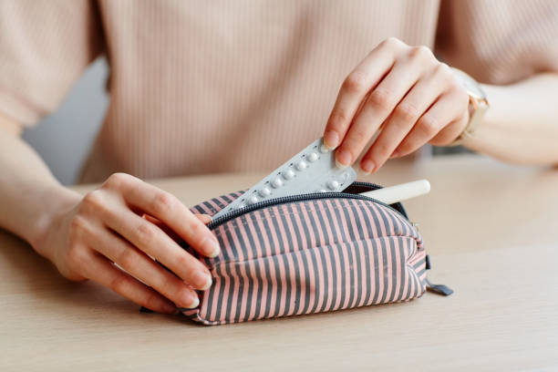 Birth Control in Travel Bag Minimal close up of young woman putting birth control pills in purse and other feminine essentials contraceptive stock pictures, royalty-free photos & images
