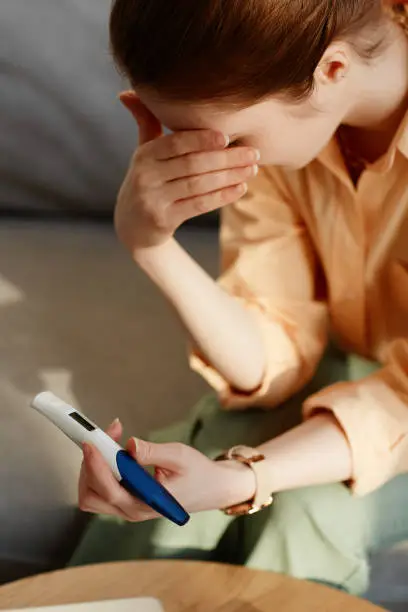 Vertical closeup of crying young woman holding pregnancy test at home and covering eyes