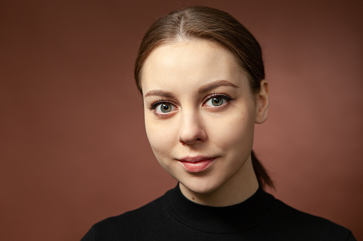 Close up studio portrait of an attractive 20 year old woman with brown hair in a black longsleeve on a brown background