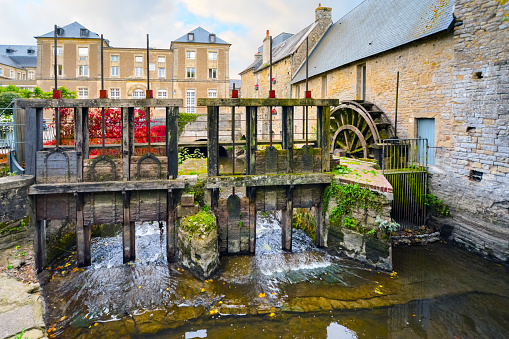 A wooden water wheel turns water along the River Aure at an old stone mill in Bayeux, France, in the Normandy region.
