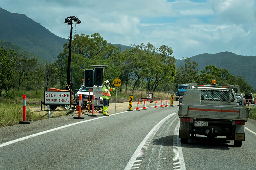 Townsville, Queensland, Australia - May 2022: Road worker holds a slow sign during road works on the highway.