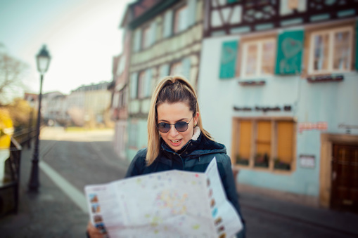 A beautiful female tourist in France. She is holding a large city map, checking out where to go next.