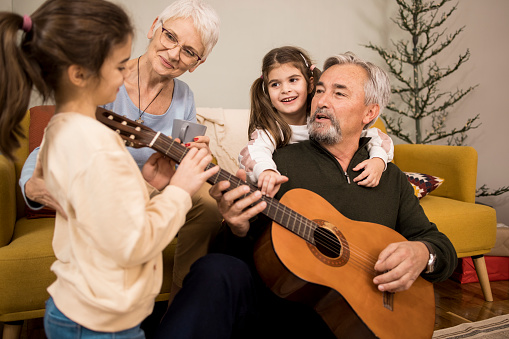 Two little sisters singing and having fun with their grandma and grandpa while grandpa playing a guitar.