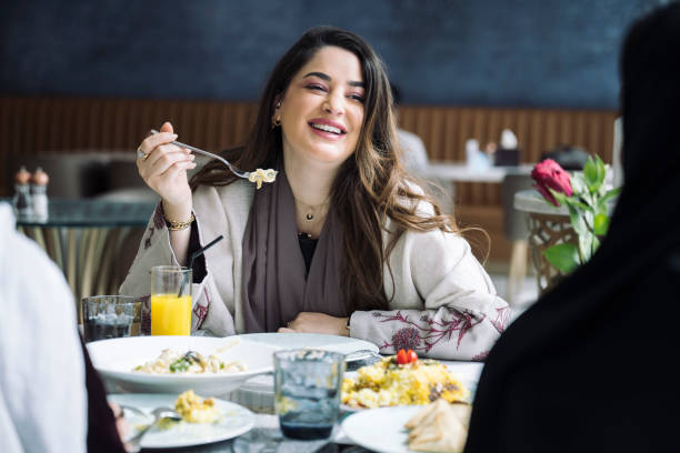 Relaxed Middle Eastern woman enjoying meal with friends In-between view of longhaired woman in late 20s pausing from eating to laugh while lunching with women in Riyadh restaurant. women only restaurant stock pictures, royalty-free photos & images